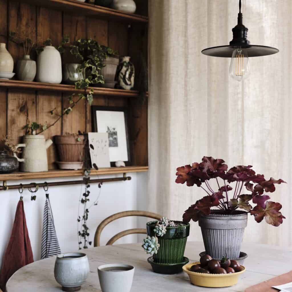 En Simona kruka i grå från Bergs Potter står på ett rustikt bord, omgiven av andra krukor och inredningsdetaljer i ett mysigt kök.