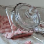 Liggande glasburk med lock fylld med rosa karameller på linnetyg – från Strömshaga hos Hemlängtan.