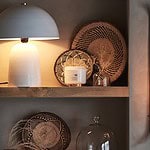 Stilfull inredning med en bordslampa, flätade korgar och väggmonterad ljushållare på en hylla, tillsammans med en glasvas från Affari of Sweden, fylld med dekorativa grässtrån.