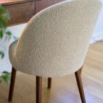 Stol BARBARA i beige bouclé vid skrivbord i trä – visar den rundade ryggen och texturen i tyget.
