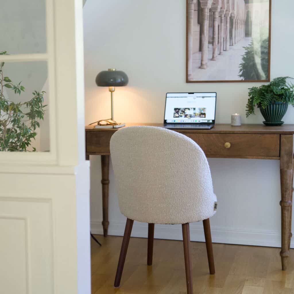 Stol BARBARA i beige bouclé vid skrivbord i trä – harmonisk hemmakontorsmiljö med varm belysning.