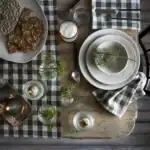 En dukning med tallrikar från serien Annabelle av Affari of Sweden. Tallrikarna är staplade och dekorerade med en grankvist. På bordet finns även en ölglas med skum, en sked, krispbröd på en tallrik, och glasbehållare med små grankvistar. Bordet är täckt med en svart- och vitrutig duk och servett.