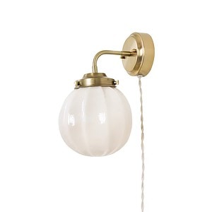 Närbild på vägglampan Marit från Strömshaga, med en kupa i opalglas och mässingsfäste. Lampan har en beige textilsladd.
