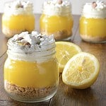 Kilner-burkar fyllda med citronkräm, toppade med grädde, maräng och nötter, bredvid halverade citroner.