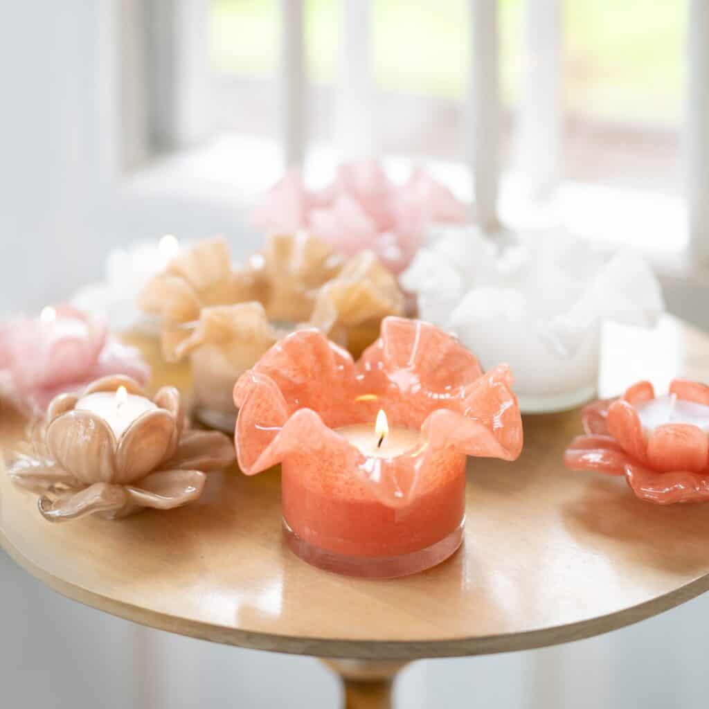 Vackra ljuslyktor i glas med mjuka pastellfärger som rosa, beige och vitt står på ett bord, och skapar en lugn och harmonisk känsla – perfekta för att fräscha upp med ljusare färger i inredningen.