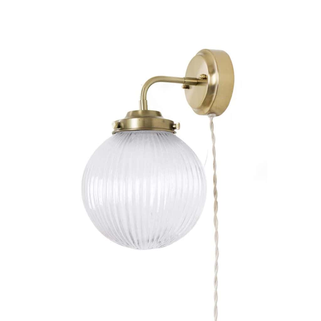 Vägglampa Eivor Mässing/Klar – en stilren lampa med mässingsfäste och räfflad glaskupa som ger ett mjukt och behagligt ljus. Perfekt för hallen, sovrummet eller vardagsrummet.