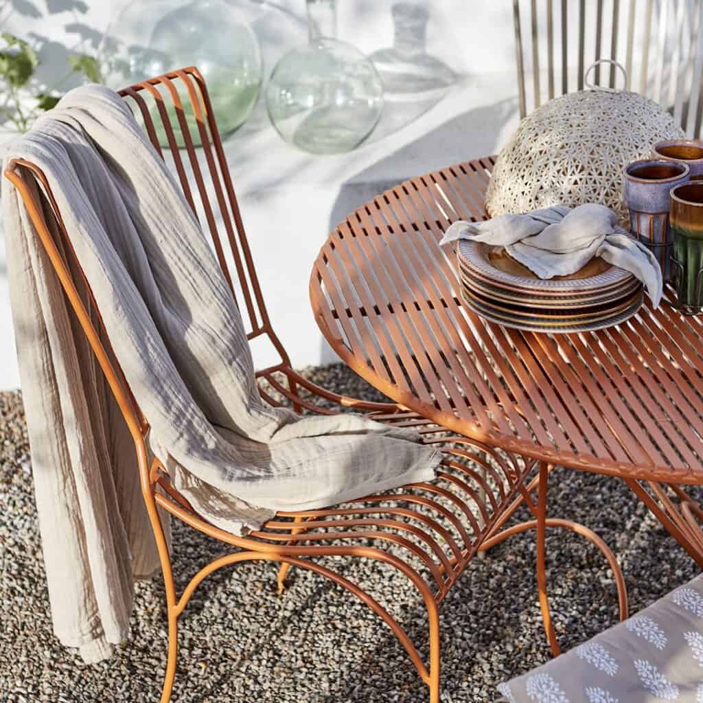 ELSA bordduk i beige bomull, elegant draperad över en stol vid ett utebord. Perfekt för avslappnade måltider i solen.