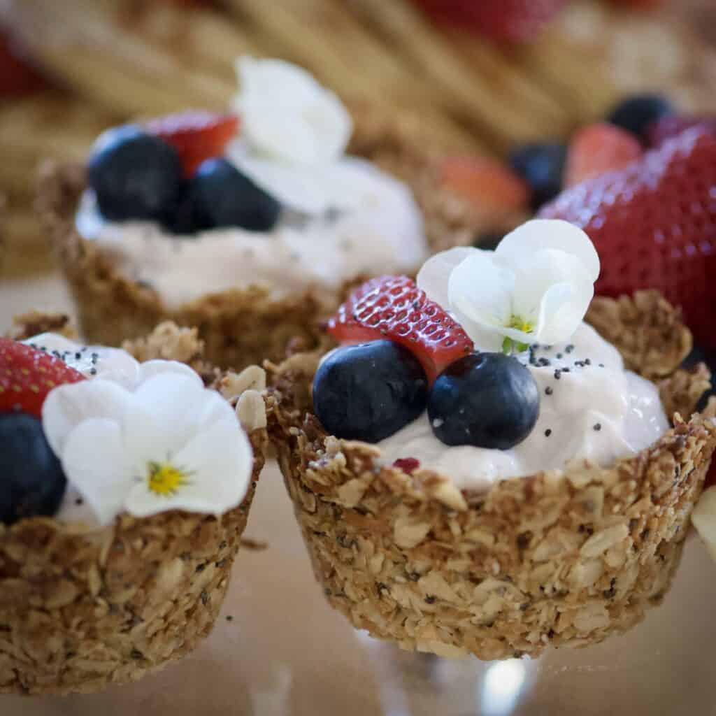Knapriga müslikorgar fyllda med krämig yoghurt och toppade med färska blåbär, jordgubbar och en ätbar blomma. Perfekt till frukost eller brunch!