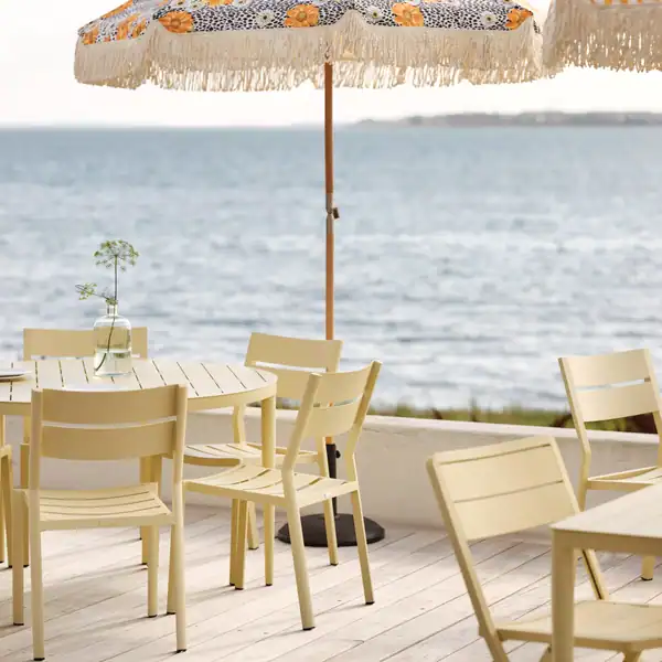 Flera DELIA matstolar i lemon uppställda runt runda bord på altan med havsutsikt.