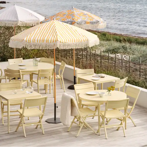 Uteservering med DELIA matstolar i lemon under färgglada parasoller vid havet.