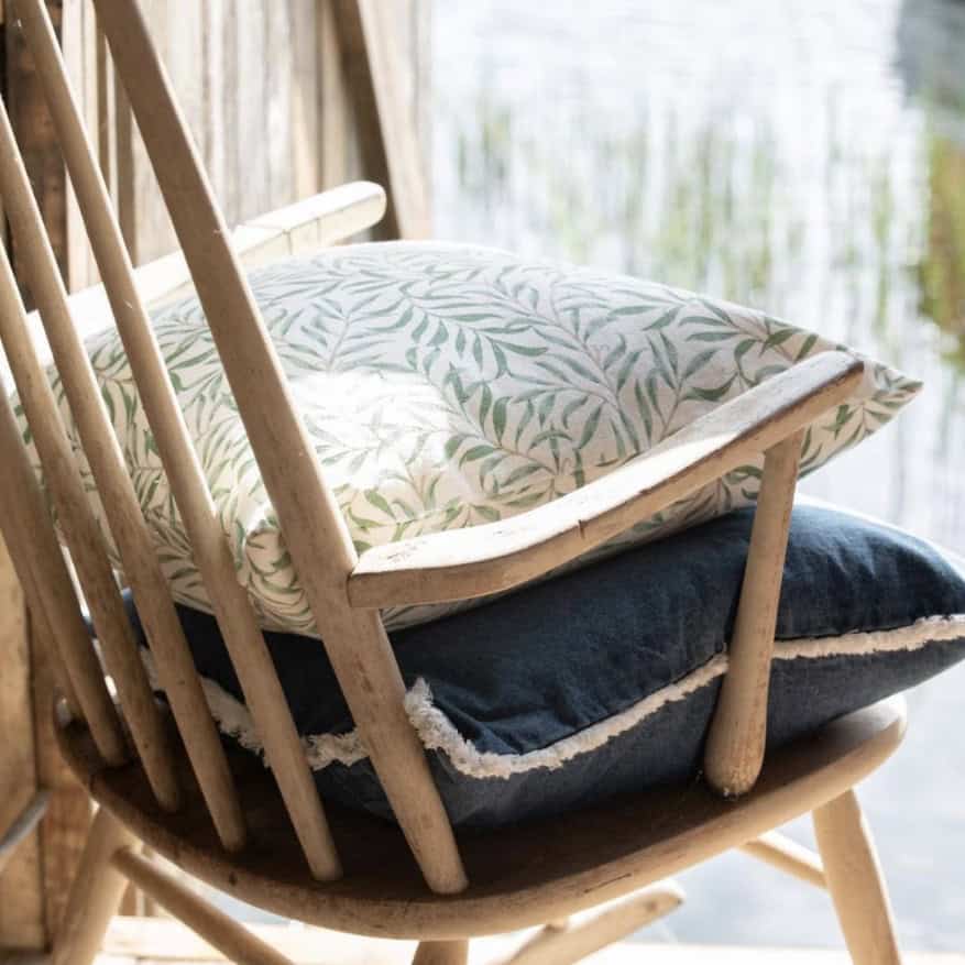 Kudde i trästol vid vattnet – inspiration för sommarstugeinredning med naturmaterial och mjuka textilier.