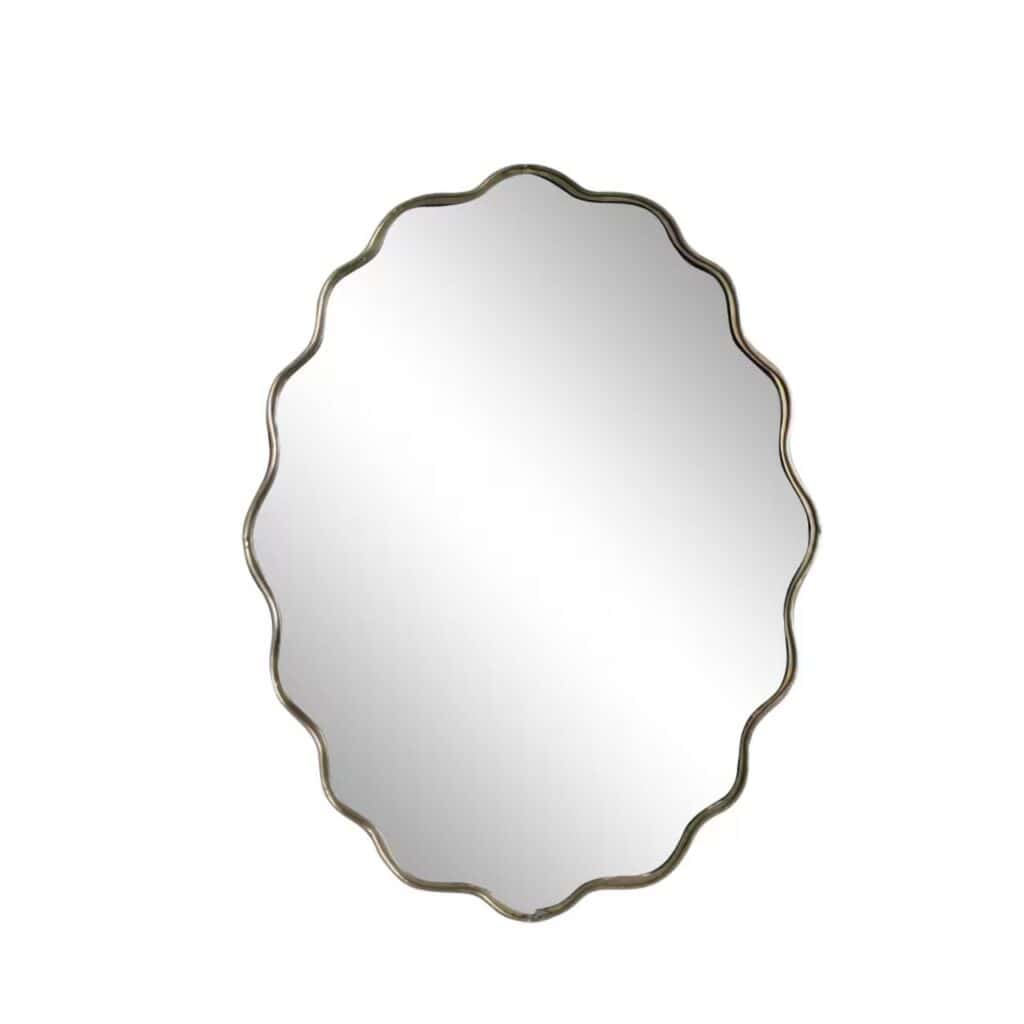 Oval spegel med vågig kant och ram i antik mässing från Strömshaga, modell Jonna, mot vit bakgrund.