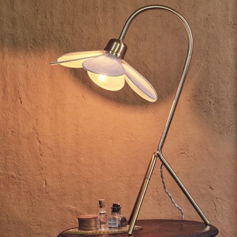 Bordslampa blomformad beige mässing från Strömshaga, tänd och placerad på träbord mot varm vägg.