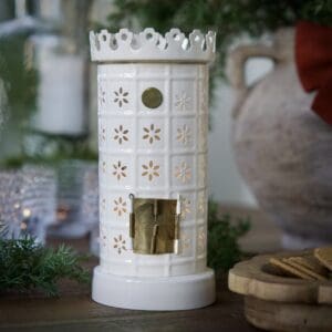 Vit ljuslykta formad som en kakelugn med utskurna blommönster, tänd i miljöbild.