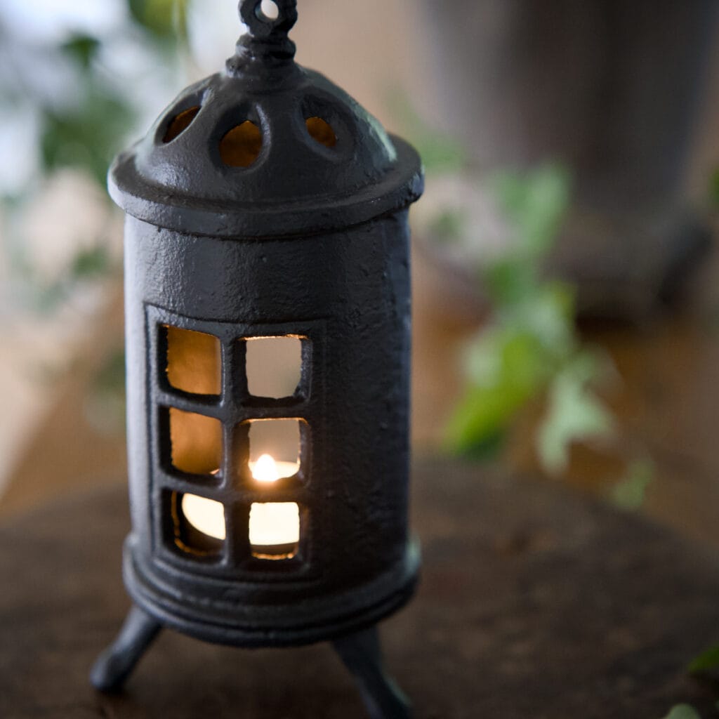 Värmeljuslykta i gjutjärn formad som en kamin med små fönster, där ett tänt ljus lyser igenom.