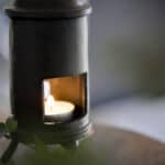 Närbild av värmeljuslykta i gjutjärn formad som en kamin, med ett tänt värmeljus synligt genom öppningen.