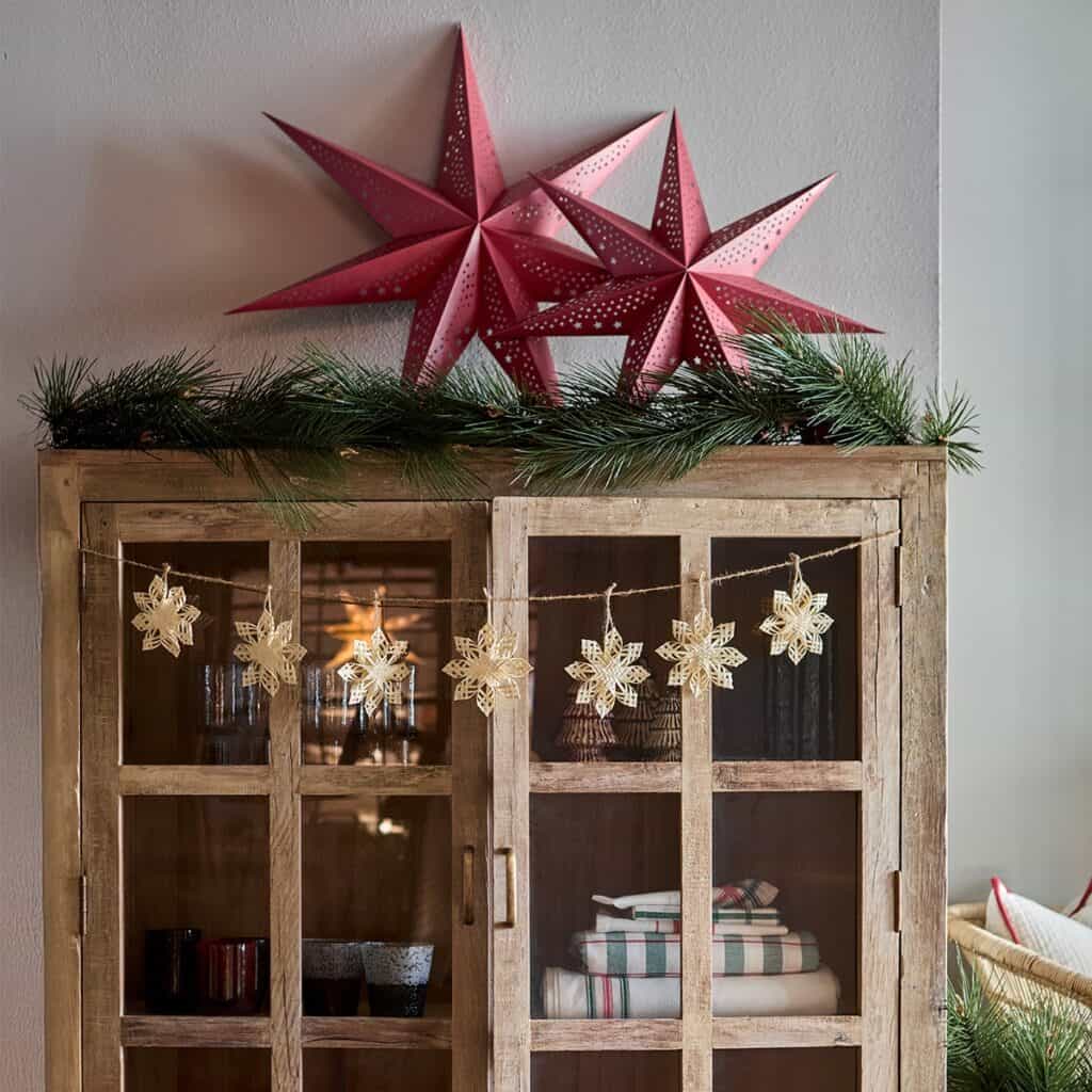Två röda julstjärnor UNI i papper på ett trähyllskåp med juldekorationer.
