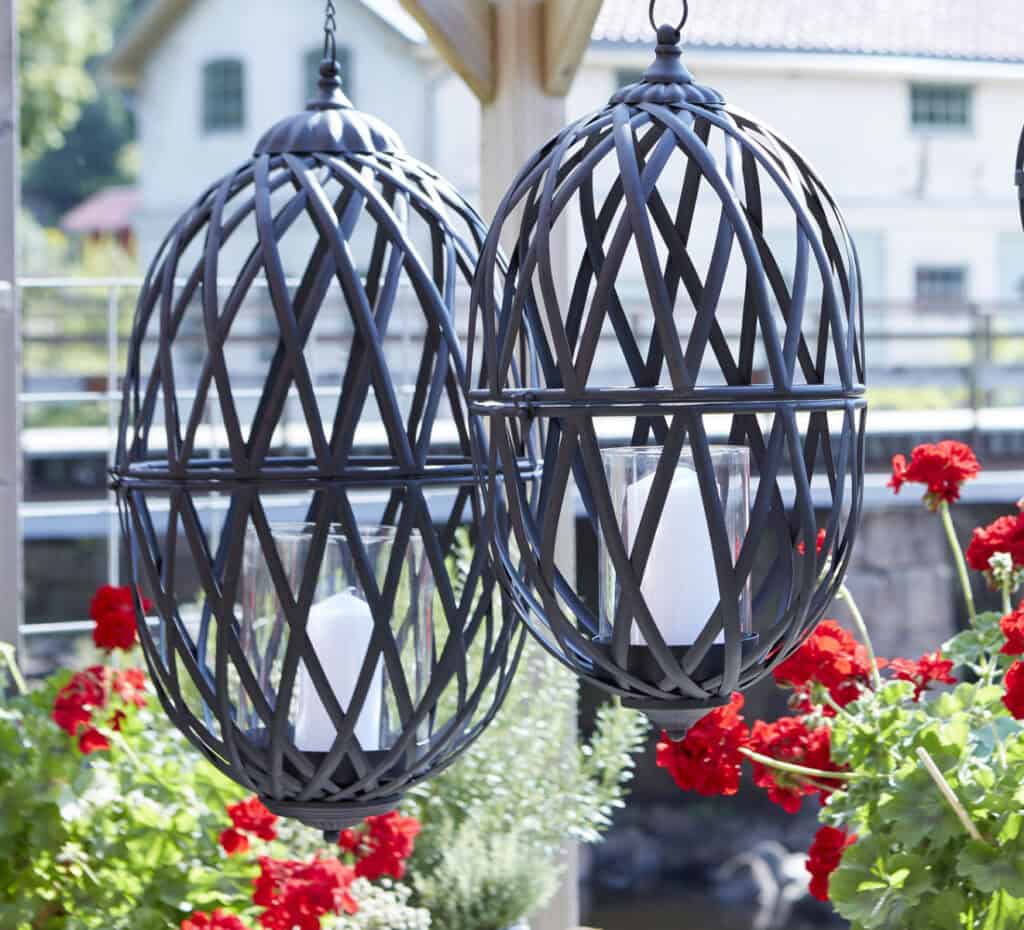 TORUN hänglyktor i antiksvart järn upphängda utomhus bland röda pelargoner.