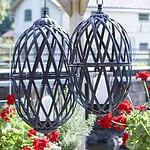 TORUN hänglyktor i antiksvart järn upphängda utomhus bland röda pelargoner.