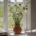 Vas i rotting med blommor placerad i fönster med dagsljus