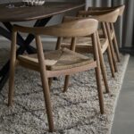 Portland karmstolar i teak med flätad sits runt ett mörkt matbord i naturlig miljö