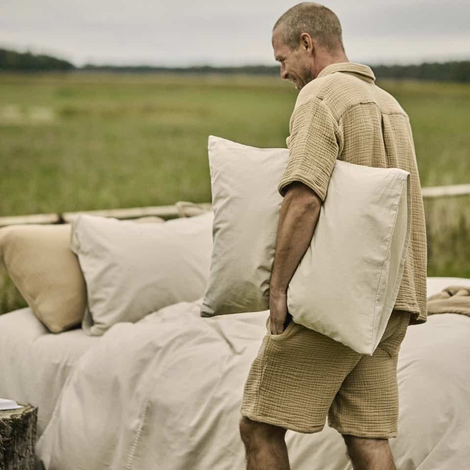 Man bär Pyjamas NICOLA nougat i 100% bomullsmuslin med kortärmad skjorta och shorts utomhus vid bäddad säng