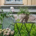 Utomhuskruka Quinn i antik terrakotta med blommor på uteplats vid trädgårdsmöbler